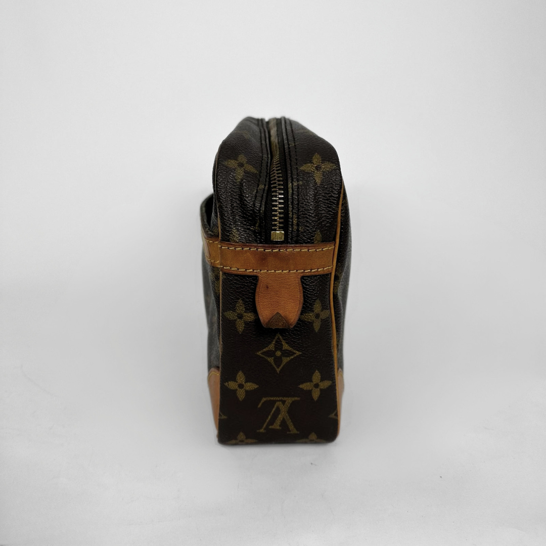 A Louis Vuitton monogram canvas toiletry bag shown from the side, featuring dark brown coated canvas with tan leather trim and a gold-tone zipper.
