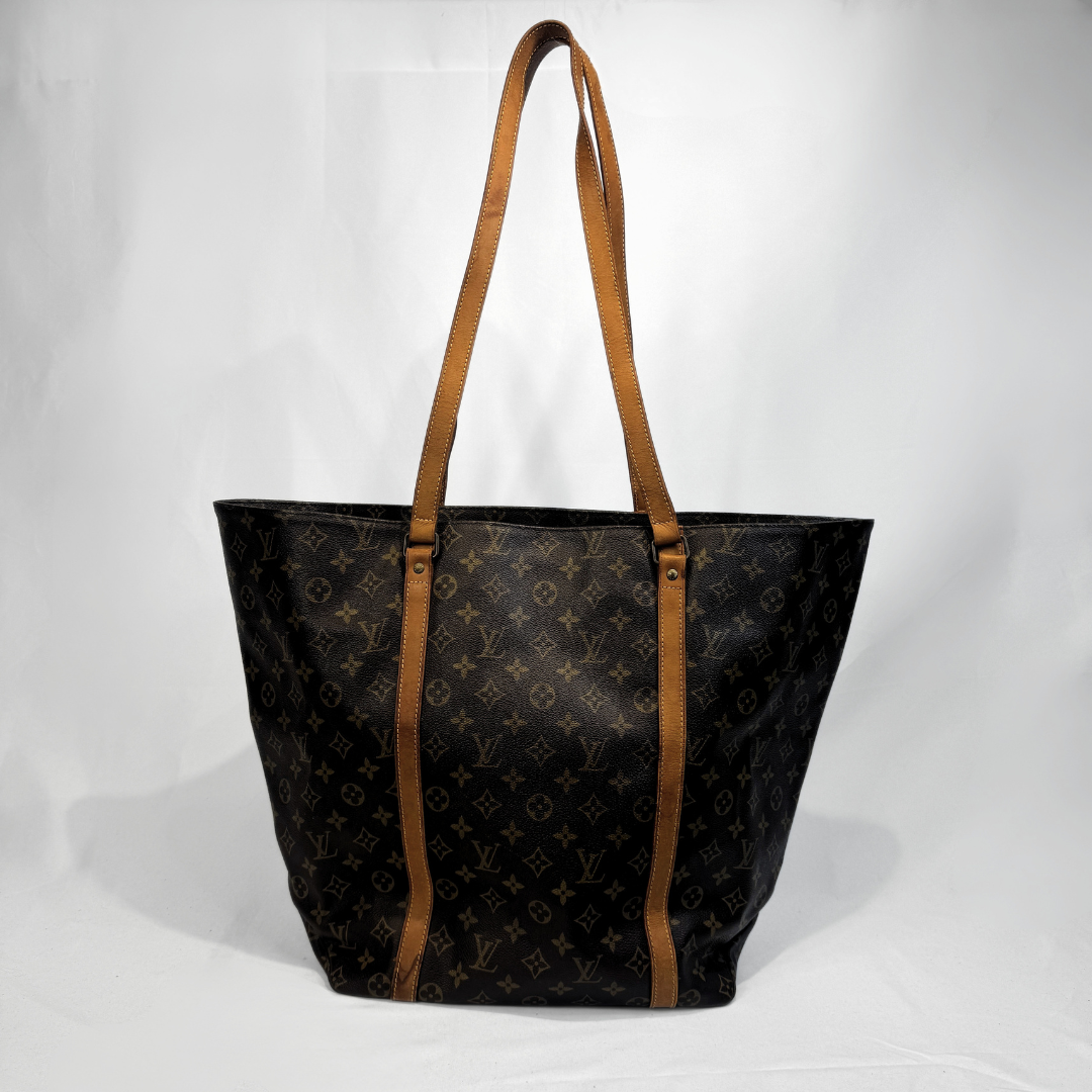 A Louis Vuitton monogram tote bag in black coated canvas with brown leather shoulder straps, photographed against a white studio background.