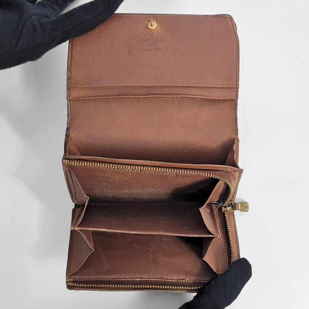 Brown leather wallet with gold zipper held by a gloved hand on a white background