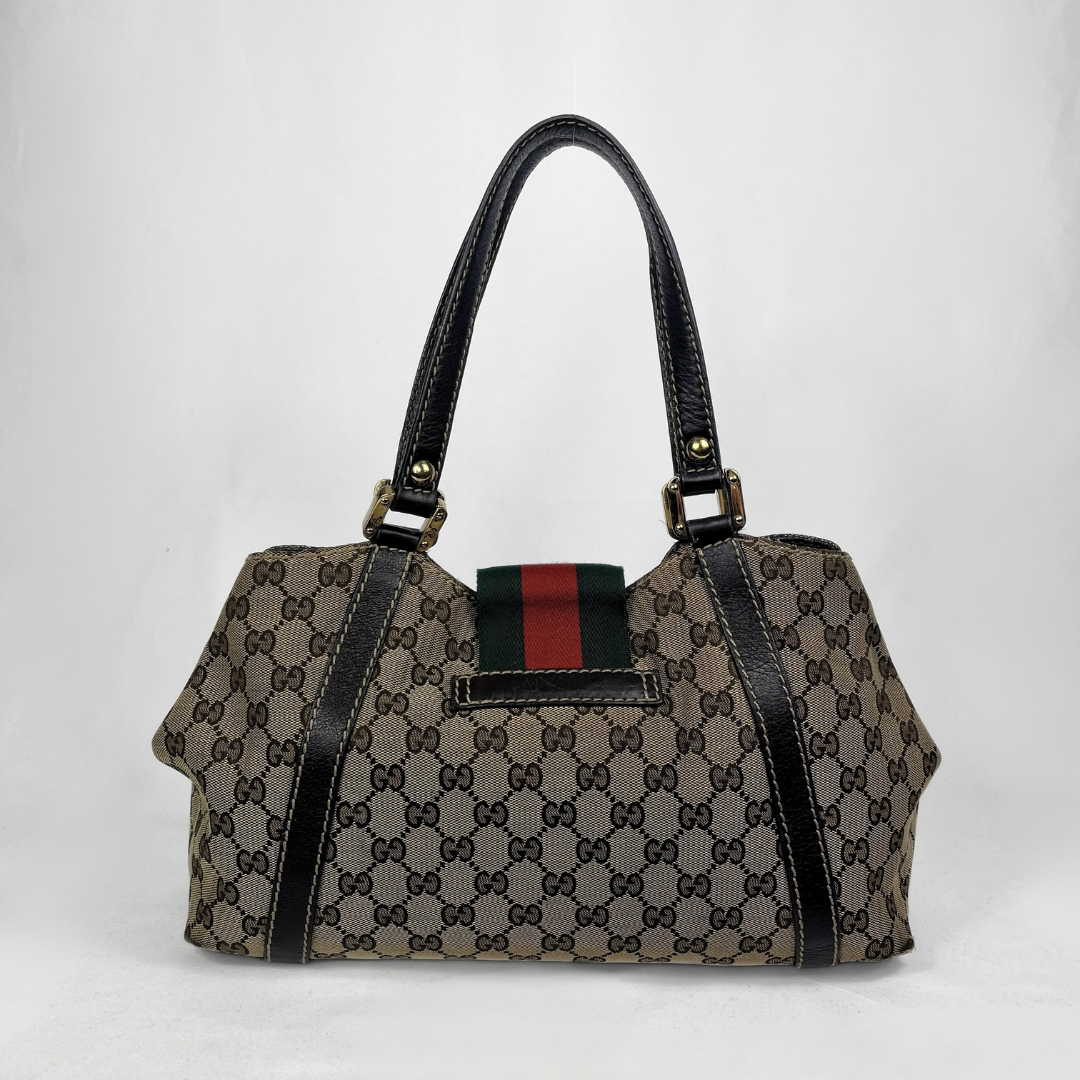A vintage-style Gucci handbag in brown GG Supreme canvas with black leather trim, double shoulder straps, and a signature green and red web stripe detail on the front.