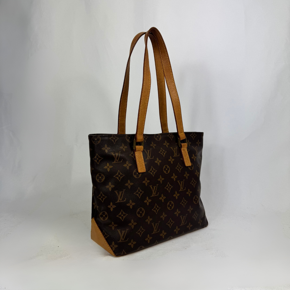 A Louis Vuitton monogram canvas tote bag with tan leather shoulder straps and trim, standing on a white studio background.