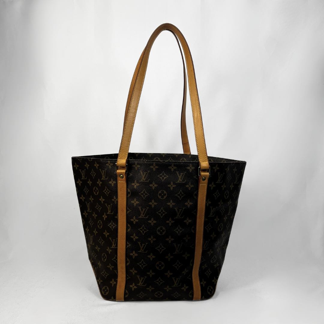 Louis Vuitton monogram canvas tote bag with tan leather shoulder straps and trim, photographed against a light gray studio background.