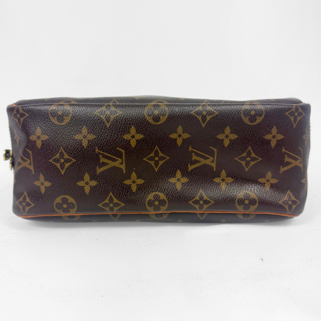 A Louis Vuitton monogram canvas toiletry bag in dark brown with gold-tone monogram prints, shown from a front-facing perspective on a white background.