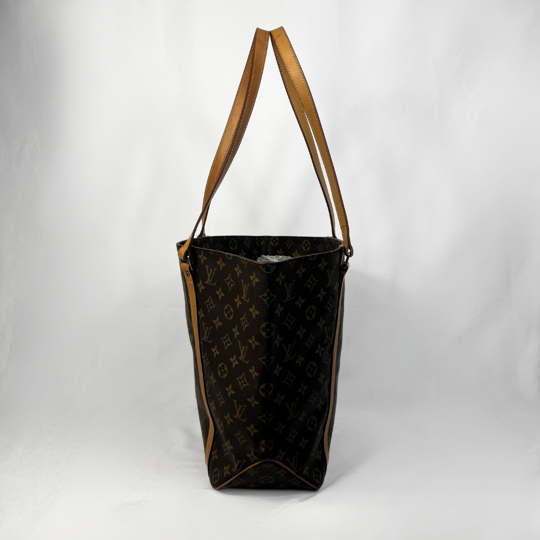 A Louis Vuitton monogram canvas tote bag with brown leather shoulder straps, standing upright against a white studio backdrop.