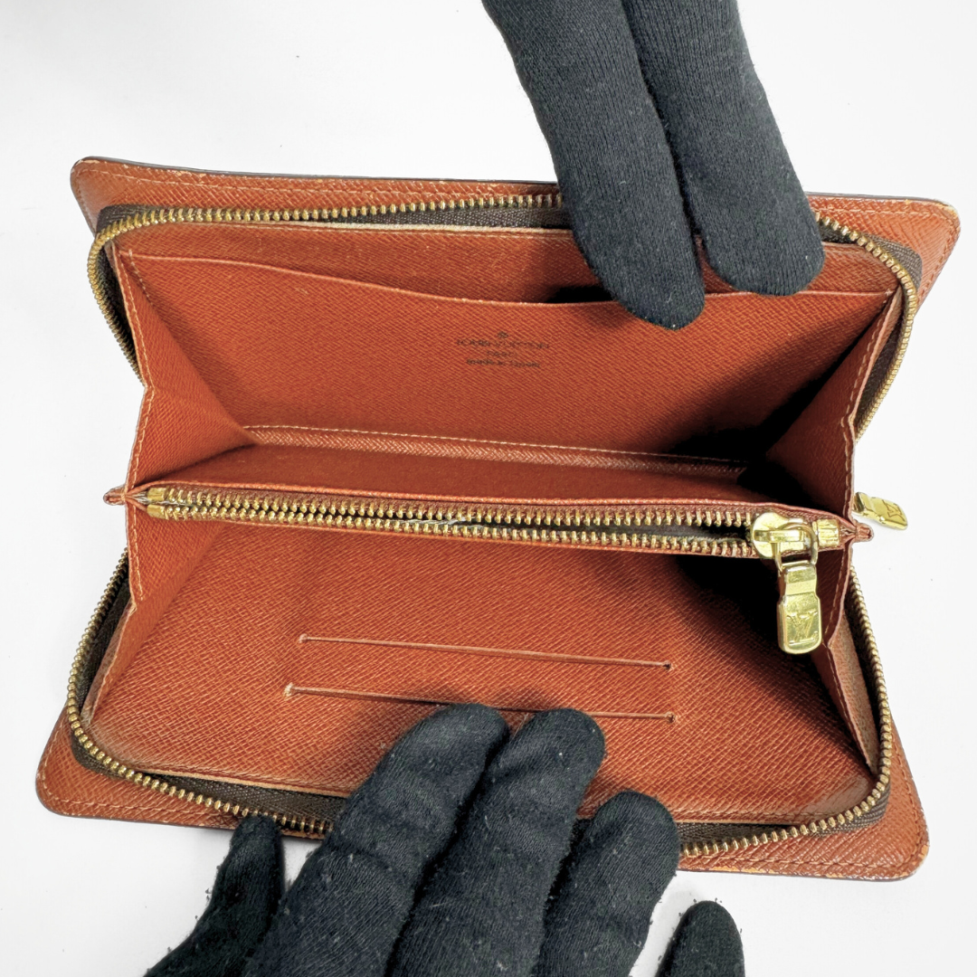 Brown leather wallet with gold zipper held open by a gloved hand on a white background