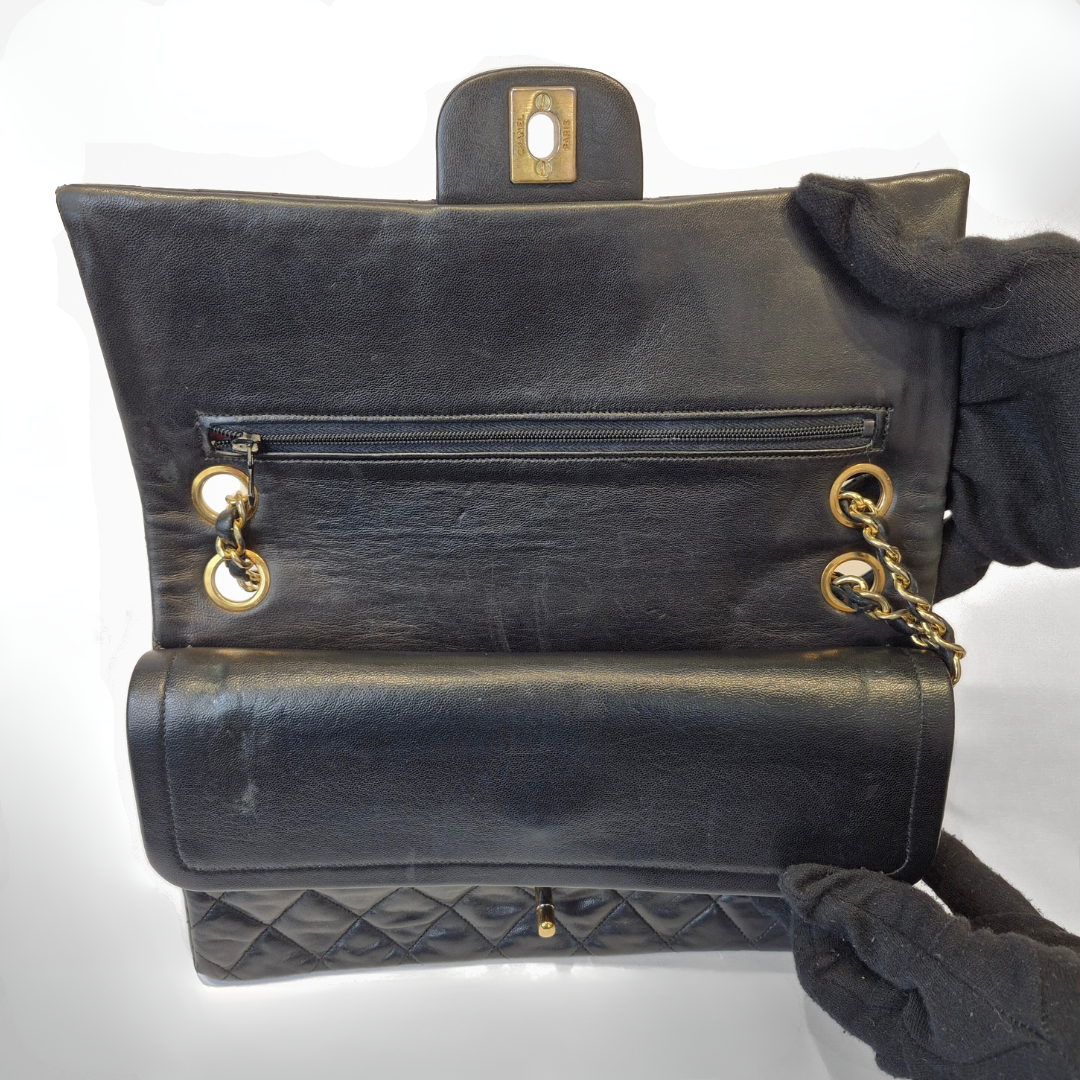 Black Chanel handbag with gold chain handle and clasp on a white background