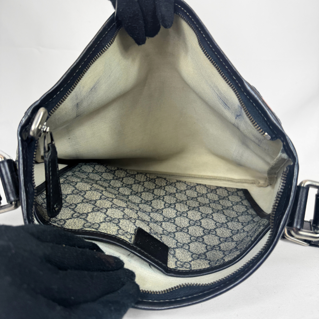 Gucci GG Supreme Web Flat Messenger bag in signature monogram canvas with green and red Web detailing and leather trims, displayed on a light grey background.