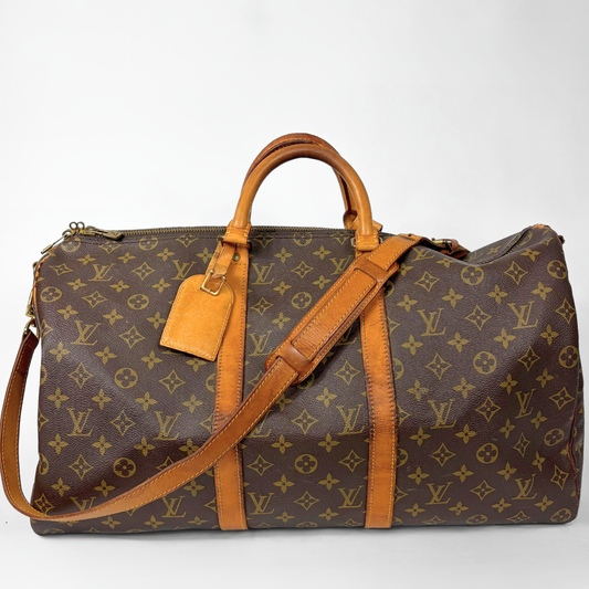 Brown monogram patterned travel bag with tan leather handles and strap on a white background