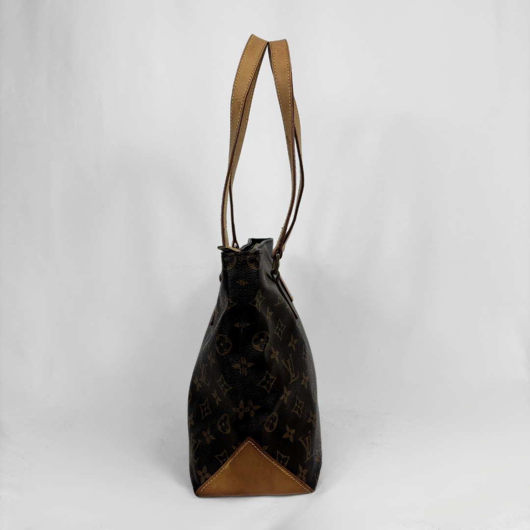 A Louis Vuitton monogram canvas bucket bag with tan leather trim and shoulder straps, shown against a plain light gray background.
