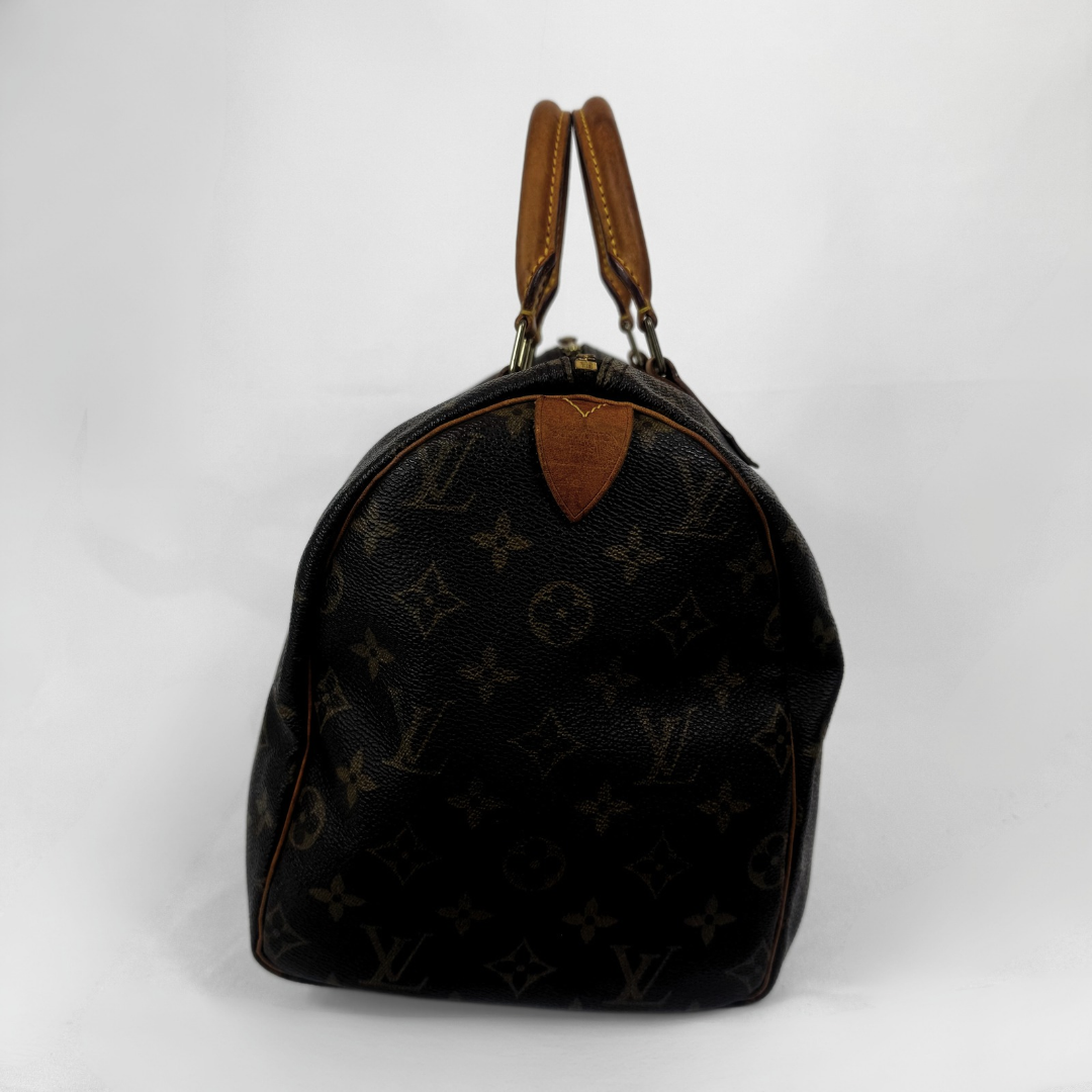 A Louis Vuitton monogram Speedy bag in black coated canvas with brown leather handles and trim, photographed against a plain white background.