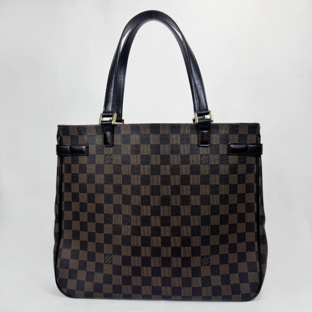 A Louis Vuitton tote bag in the Damier Ebene checkered pattern, featuring dark brown and black checkered canvas with black leather handles and trim, and gold-tone hardware.
