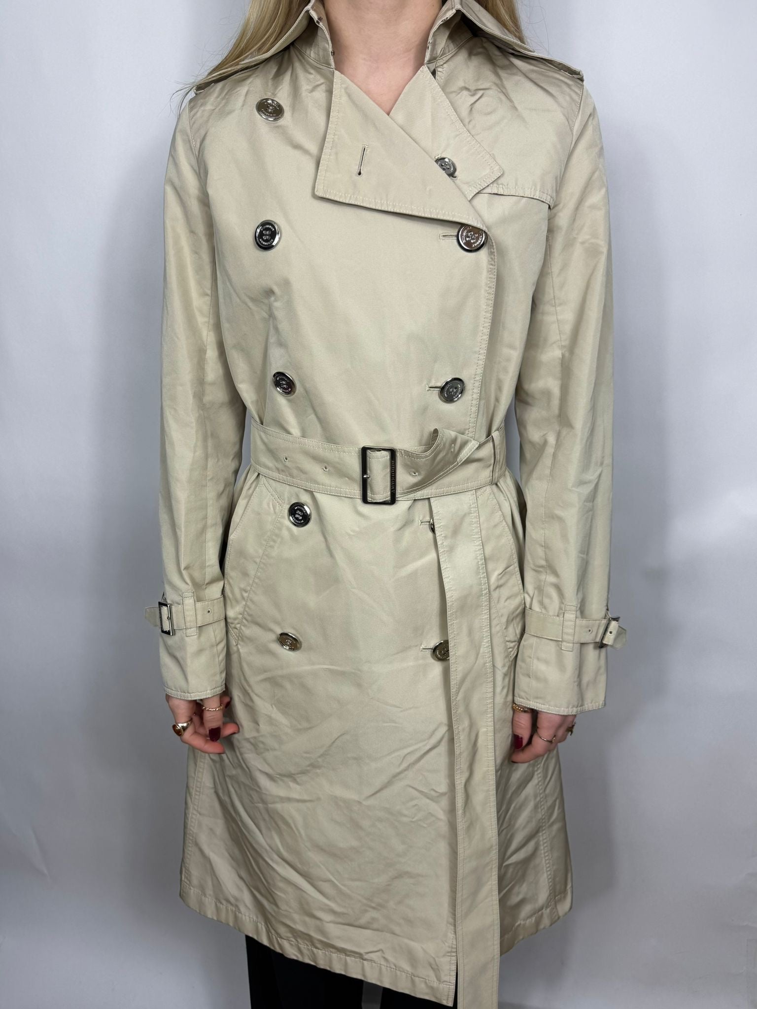Beige trench coat worn by a person on a white background